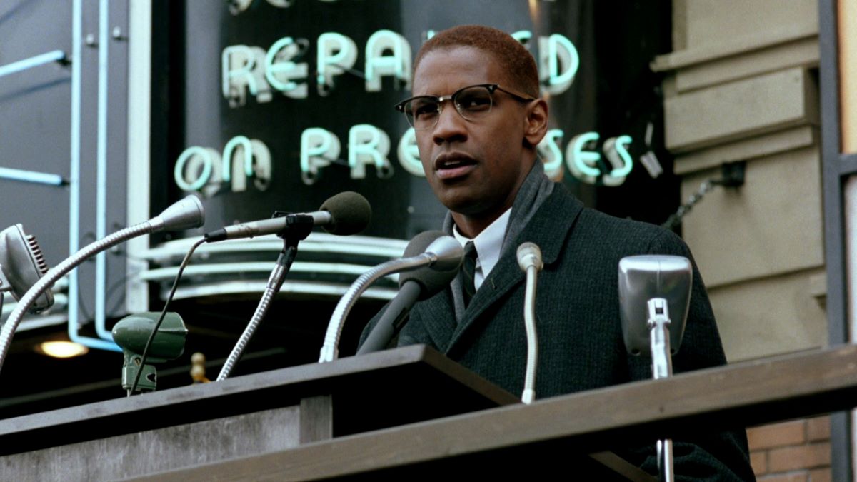 Malcolm X speaking in front of people on a street.